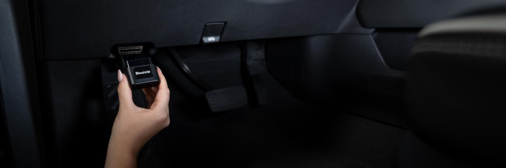 A hand plugging the Bouncie device into a vehicle's OBD2 port